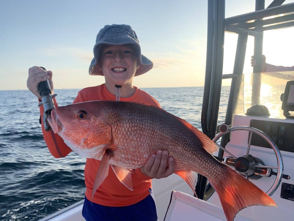 A young boy showing off his catch with Reel Rosie Fishing Charters - one of the top outdoor activities in Panama City beach
