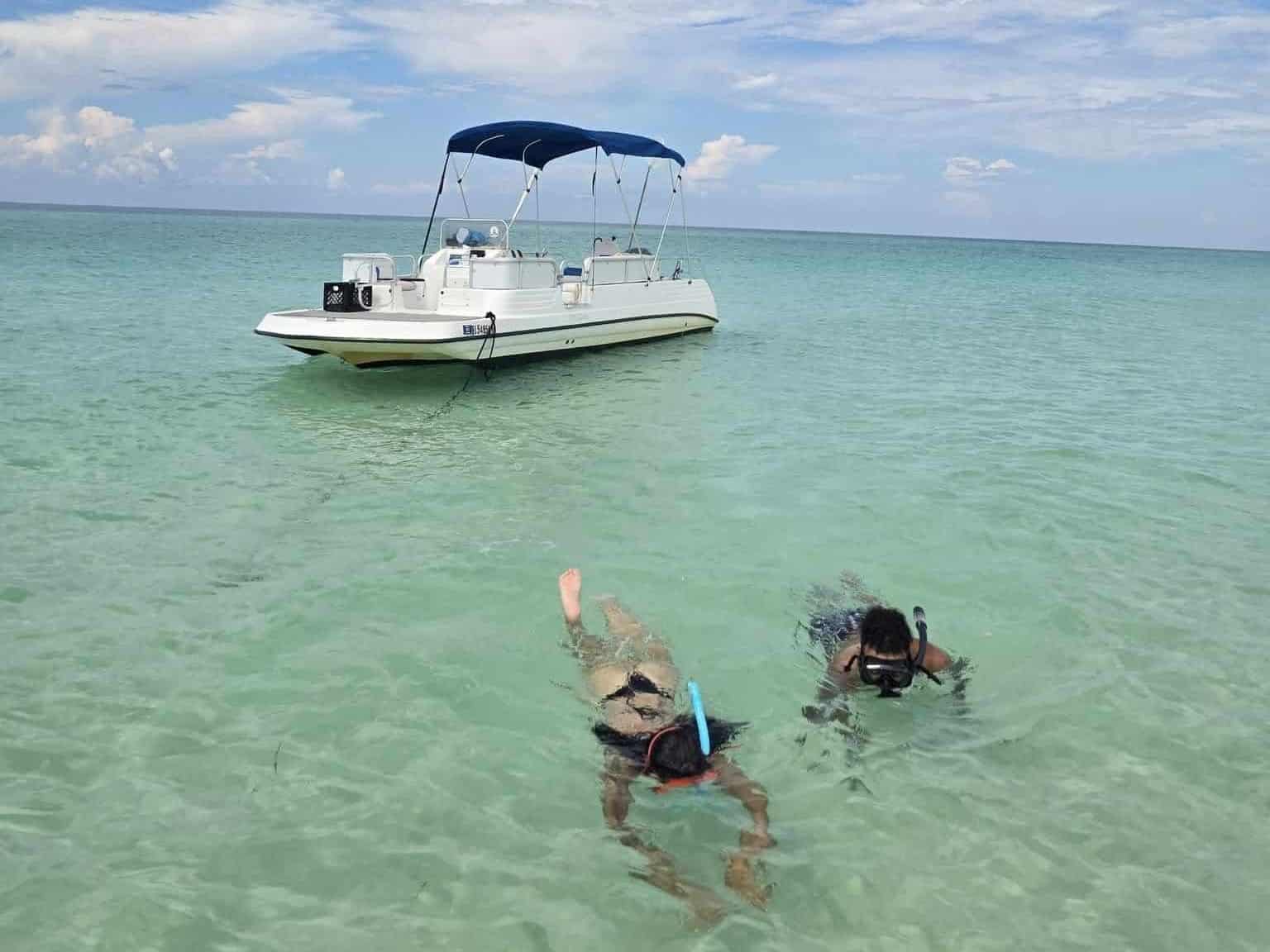 Two people snorkeling near a private boat in shallow, clear water—enjoying one of the top outdoor activities in Panama City Beach near Shell Island.