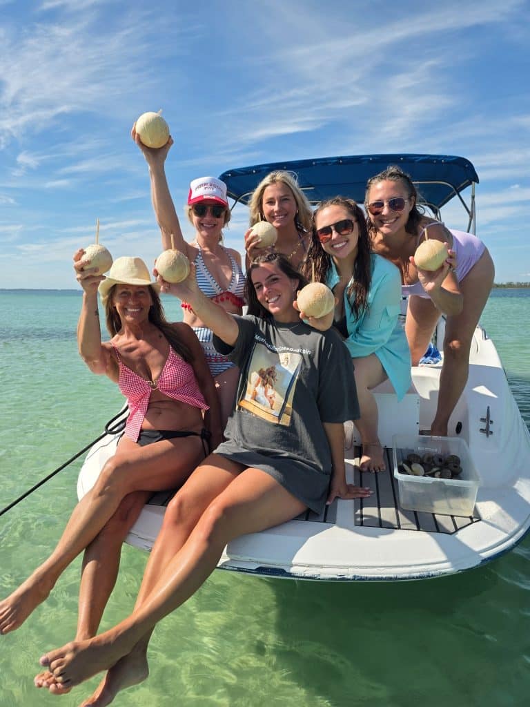 Group of women holding fresh coconuts aboard a private boat tour near Shell Island in Panama City Beach.
