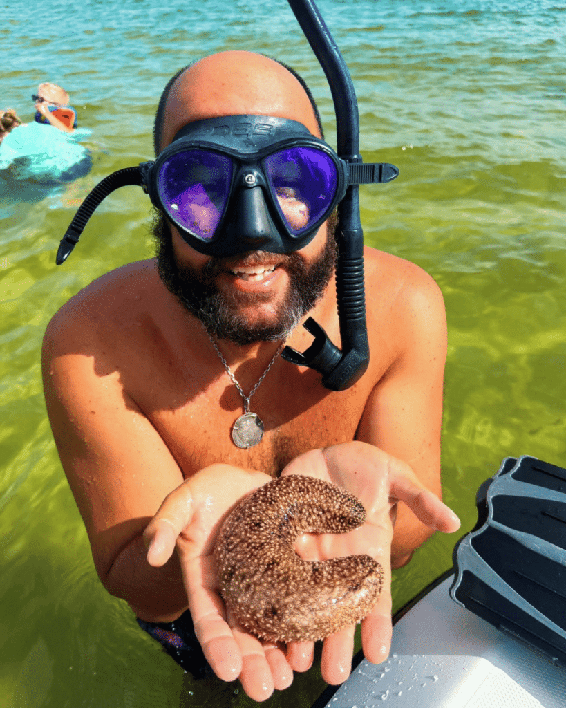 A snorkeling guest holding a sea cucumber discovered while snorkeling in the clear waters of St. Andrews Bay near Shell Island, Panama City Beach