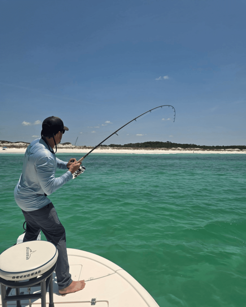 An angler fighting a tarpon fish on the bow of a boat in the emerald green Gulf waters off Shell Island during the Silver Scale Tarpon Tournament for tagging tarpon Panama City Beach